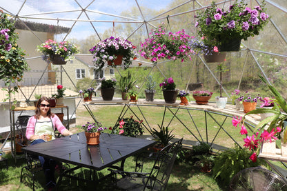 Inside photo of a 16 ft greenhouse displaying flowers and half dome built-in shelving.