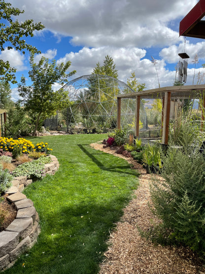 A path of perfect green grass winds between gardens,  leading to a 28 Ft aviary set against a blue sky with large puffy clouds.